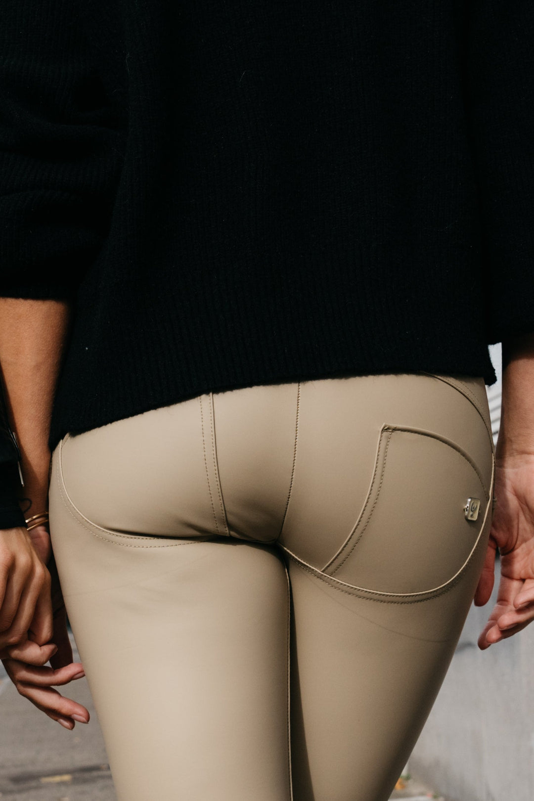 Person wearing beige pants with a black top, standing against a blurred background