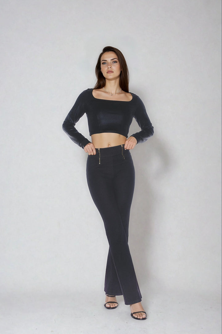 Woman wearing a black long-sleeve crop top and high-waisted pants on a white background
