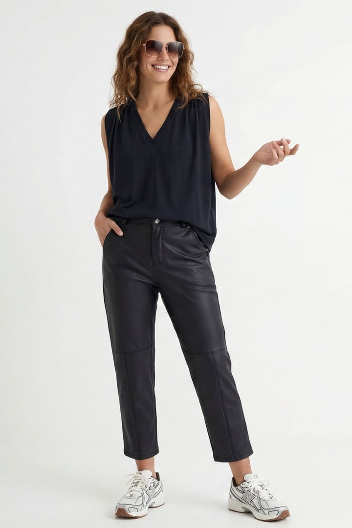 Woman wearing a black sleeveless top and dark jeans, standing against a white background.