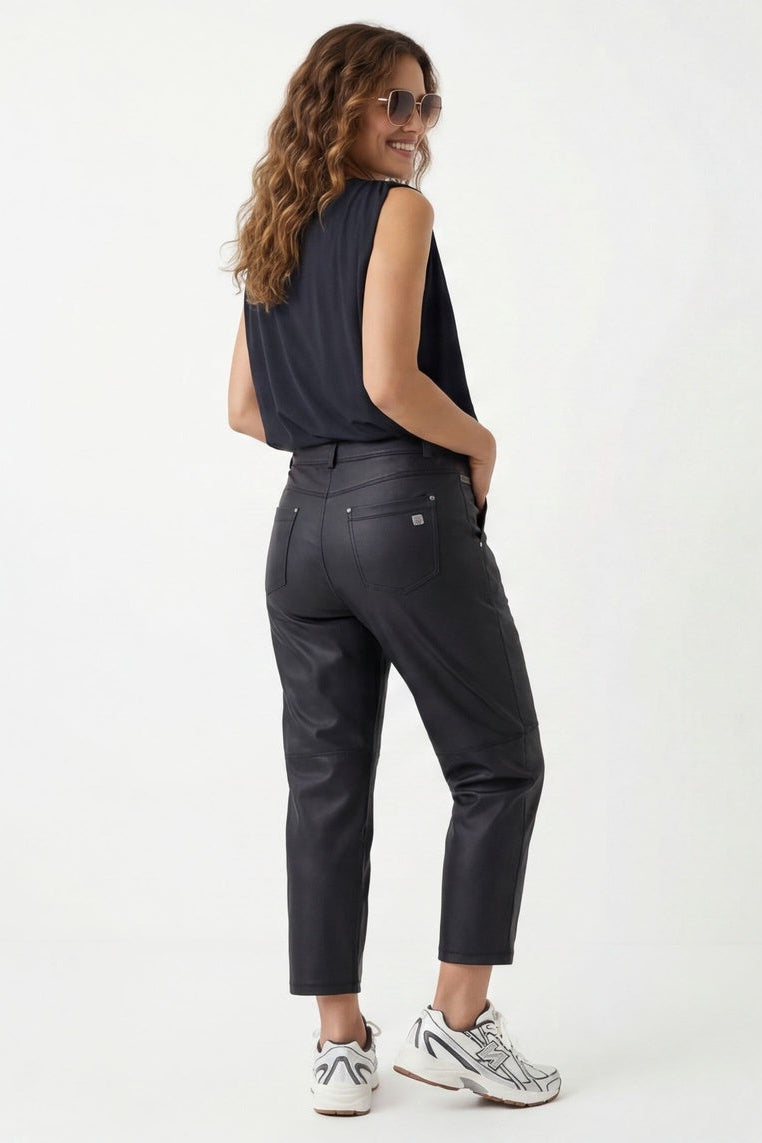 Woman wearing a black sleeveless top and dark jeans, standing against a white background.