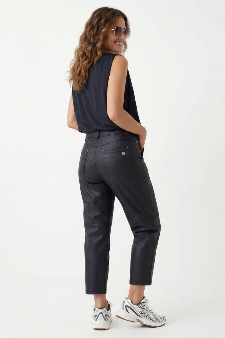 Woman wearing a black sleeveless top and dark jeans, standing against a white background.