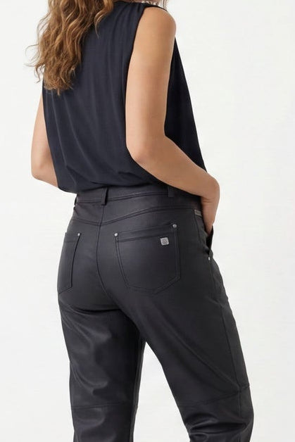 Woman wearing a black sleeveless top and dark jeans, standing against a white background.