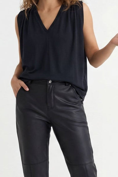 Woman wearing a black sleeveless top and dark jeans, standing against a white background.
