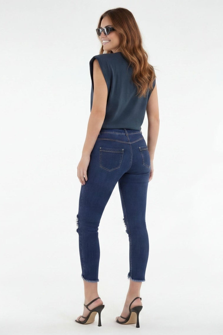 Woman wearing blue jeans and a dark top, standing against a white background