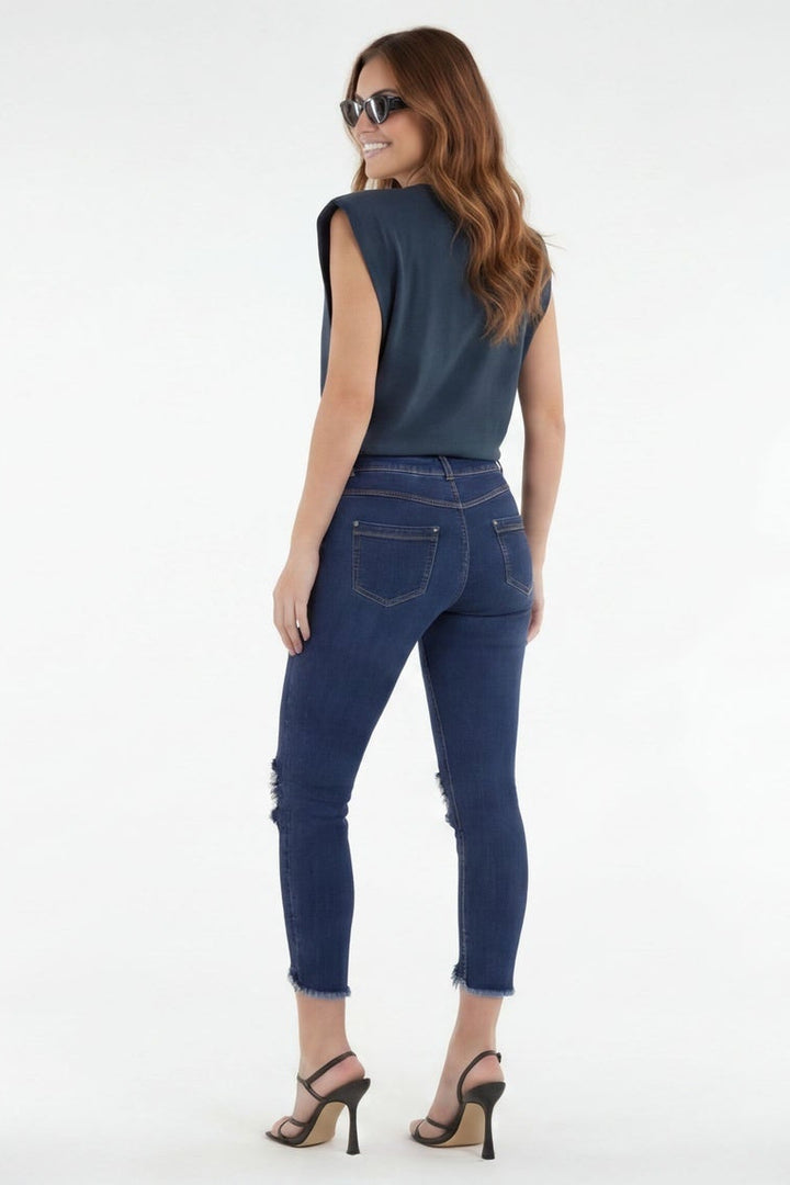 Woman wearing blue jeans and a dark top, standing against a white background
