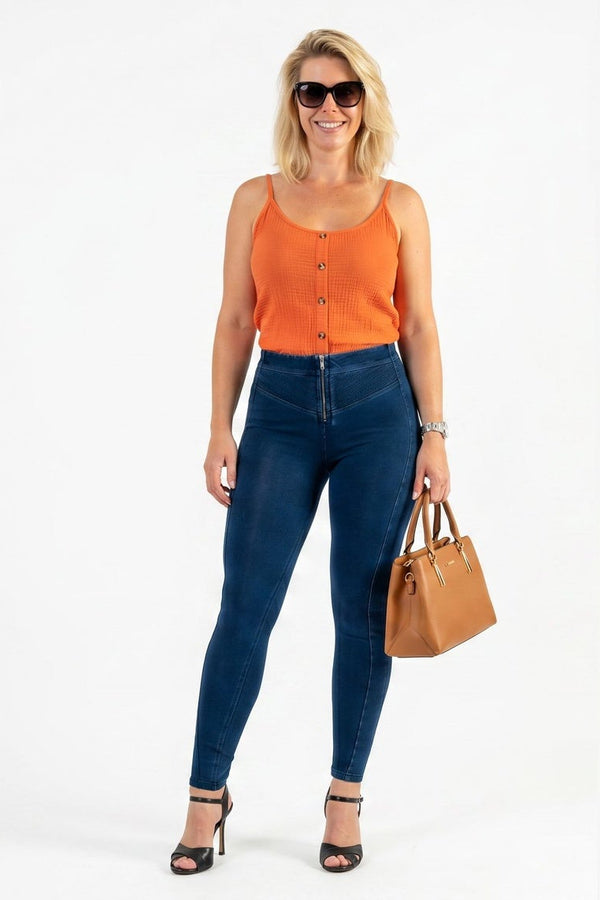 Woman wearing an orange top and blue jeans, holding a brown handbag, on a white background