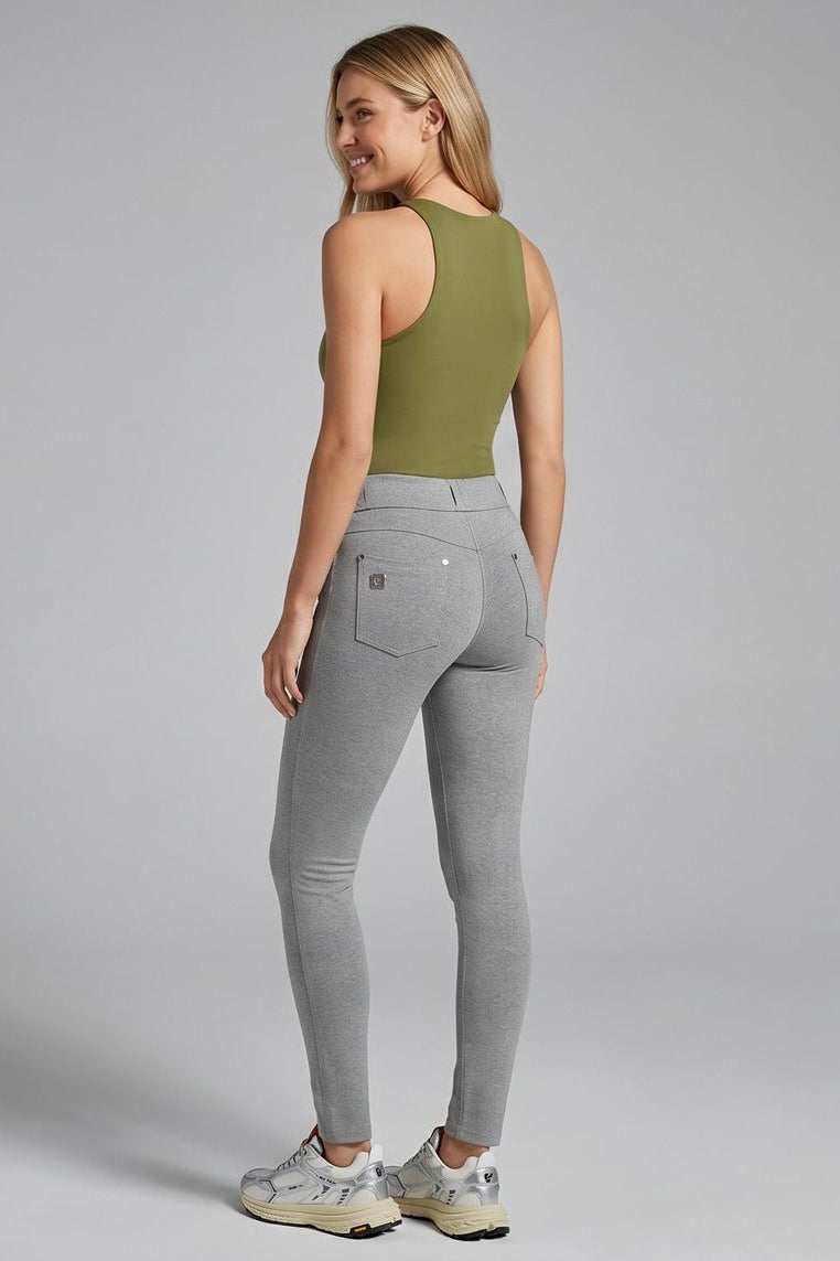 Woman wearing a green tank top and gray jeans standing against a plain background