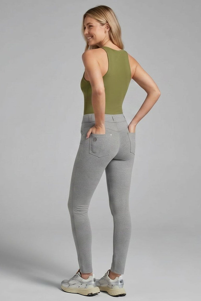Woman wearing a green tank top and gray pants, standing against a plain background.