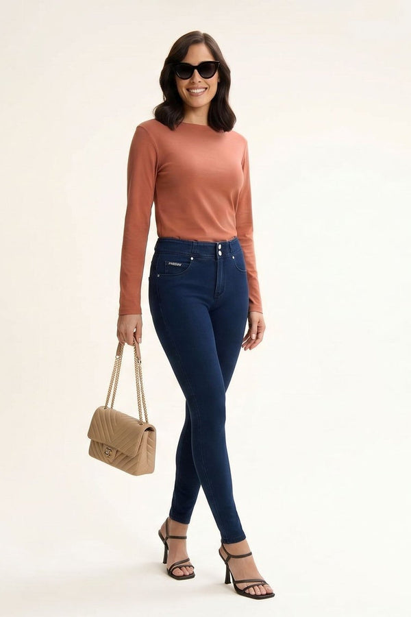 Woman modeling blue jeans with a brown top and beige handbag on a white background