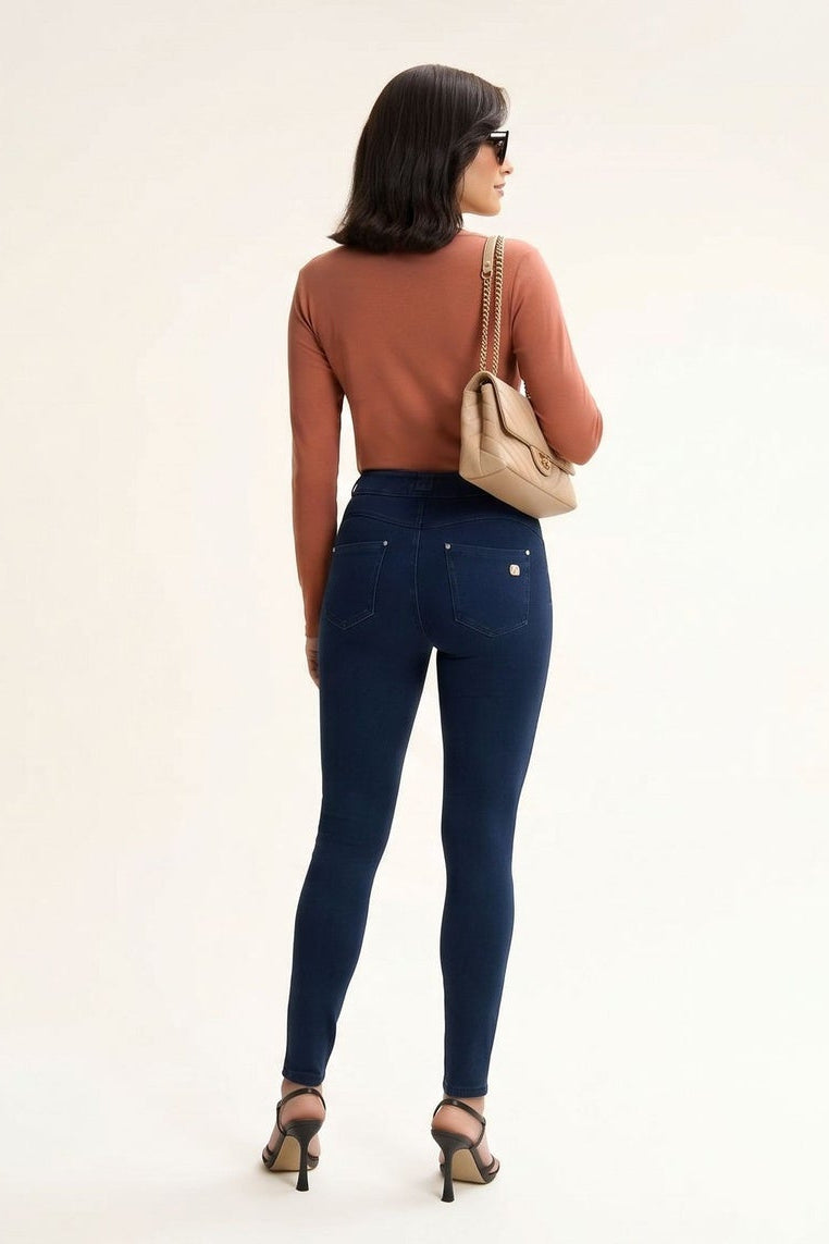 Woman modeling blue jeans with a brown top and beige handbag on a white background