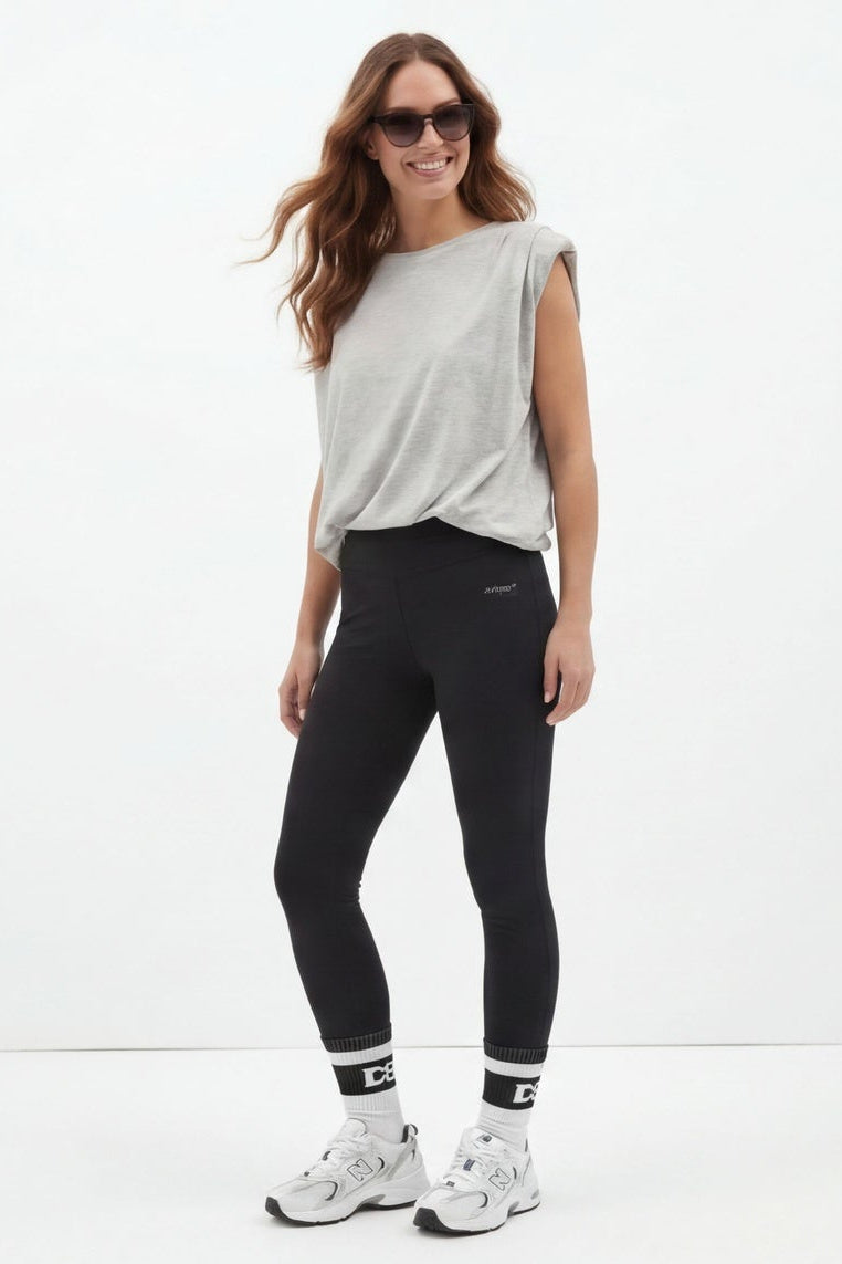 Woman wearing black leggings with a white top on a white background