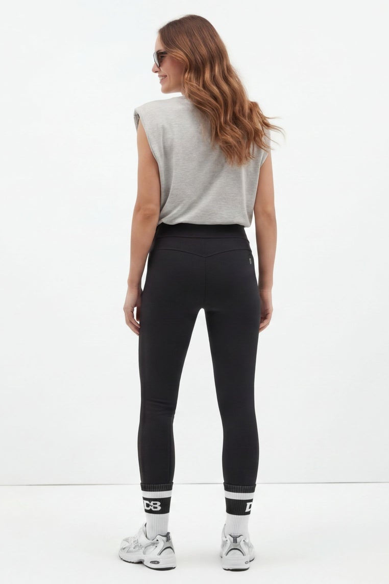 Woman wearing black leggings with a white top on a white background