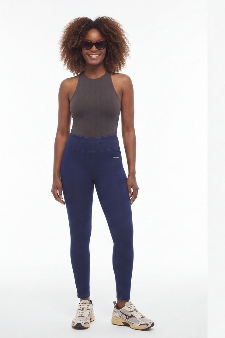 Woman wearing a gray tank top and navy leggings standing against a white background