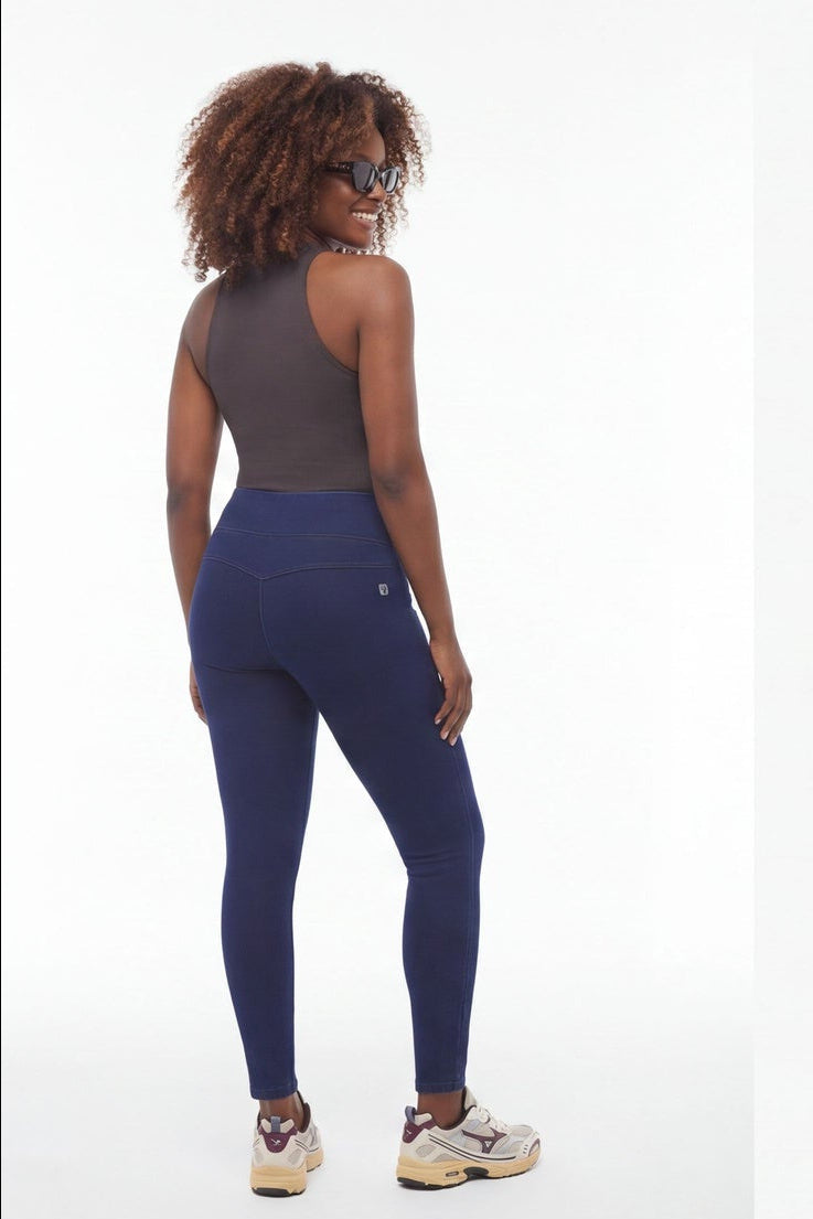 Woman wearing a gray tank top and navy leggings standing against a white background