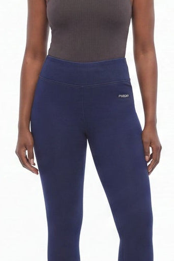 Woman wearing a gray tank top and navy leggings standing against a white background