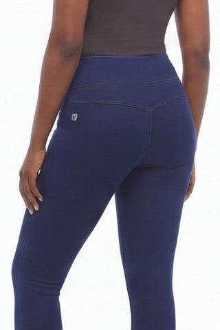 Woman wearing a gray tank top and navy leggings standing against a white background