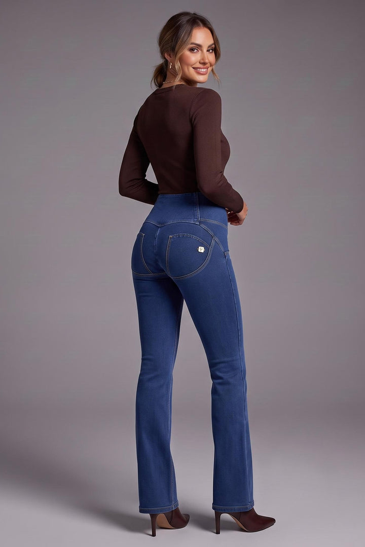 A woman wearing blue high-waisted flared jeans and a brown long-sleeve top, photographed from behind against a neutral gray studio background.