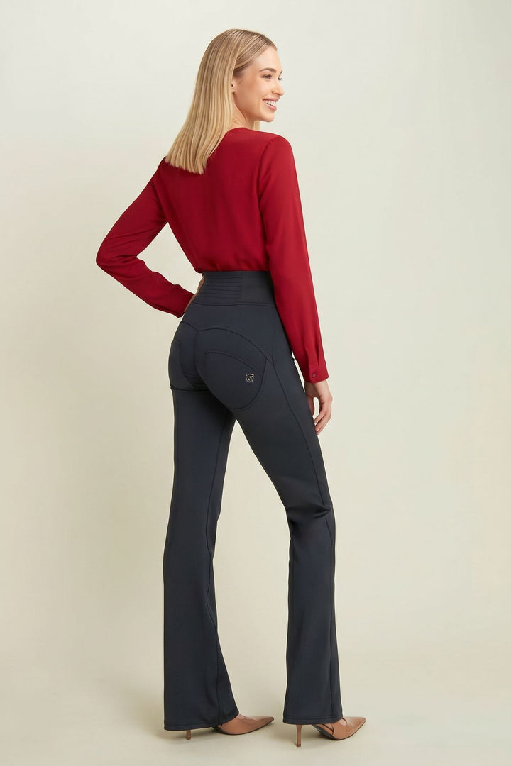 Woman wearing a red top and dark blue flared pants on a beige background