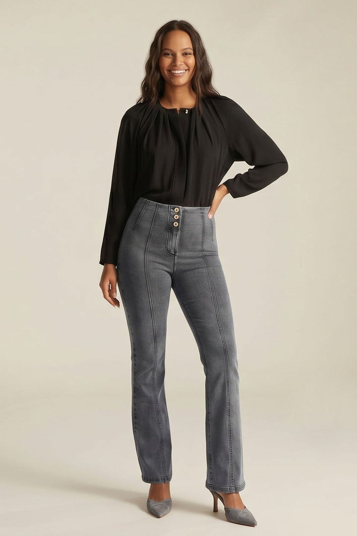 Woman wearing gray jeans and a black top, standing against a neutral background