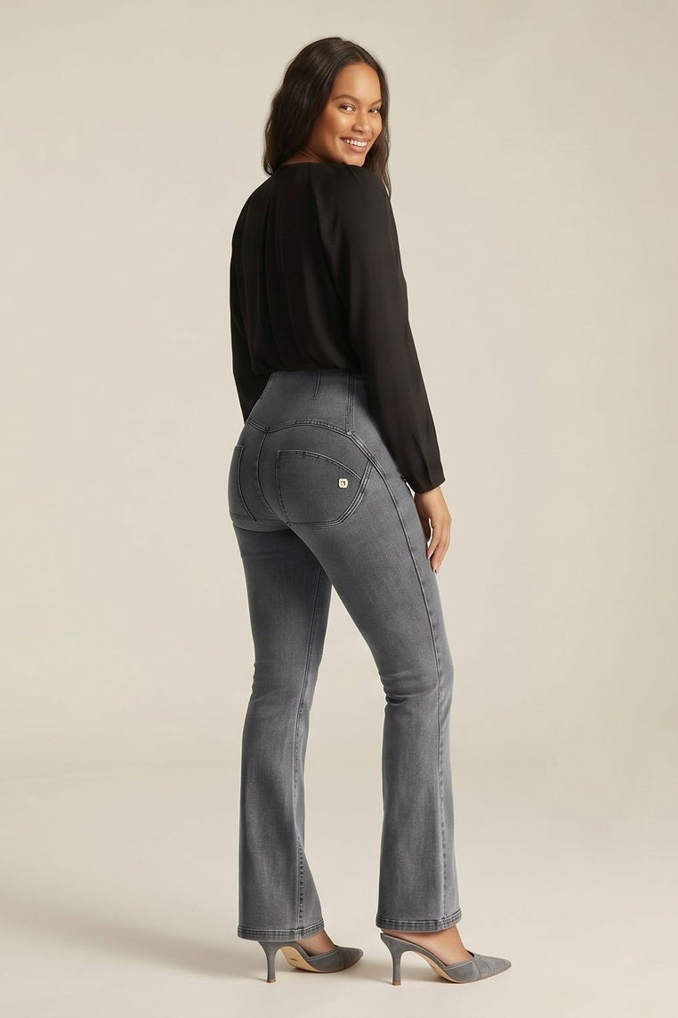Woman wearing gray jeans and a black top, standing against a neutral background