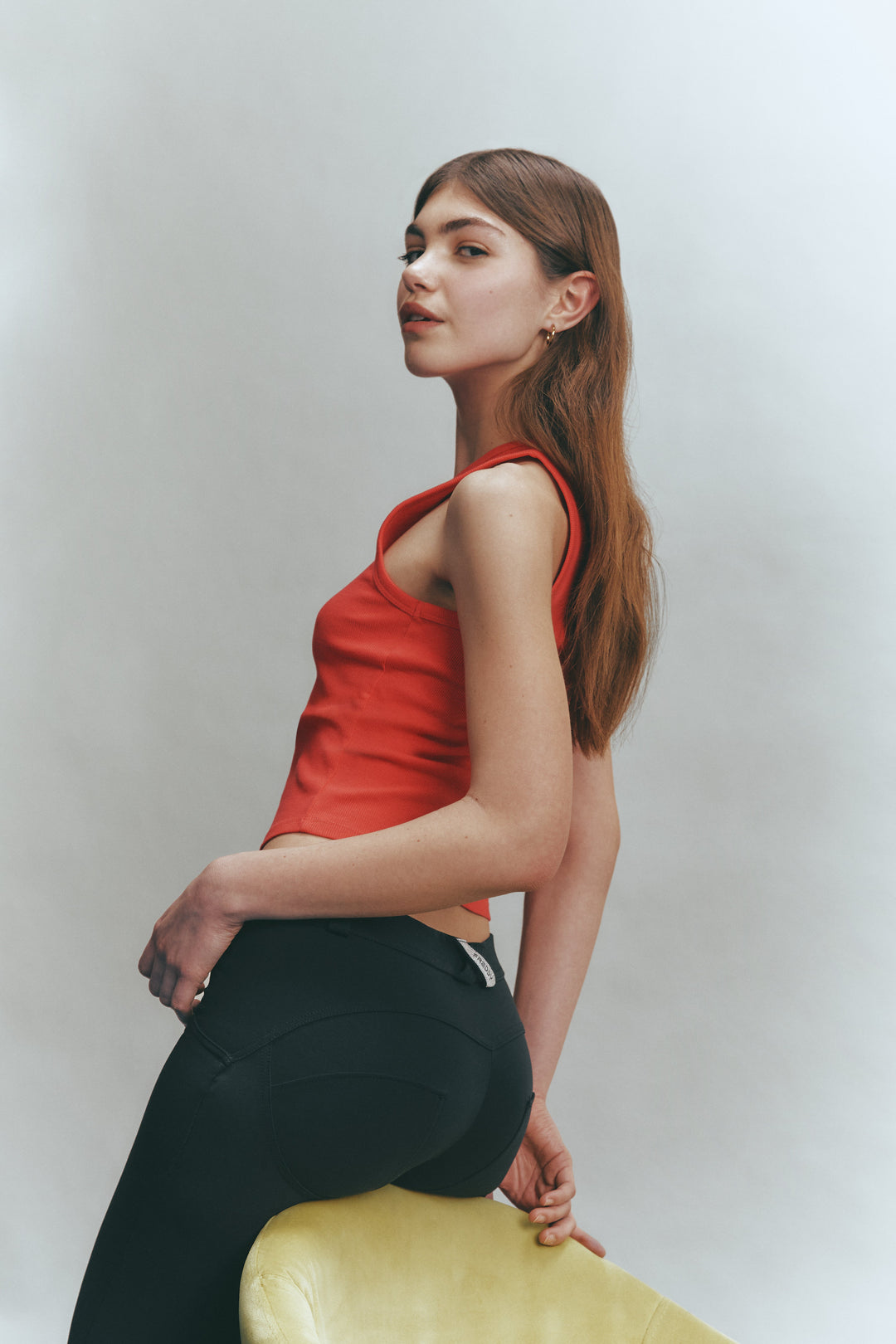Woman in a red top and black leggings sitting on a yellow ball against a plain background