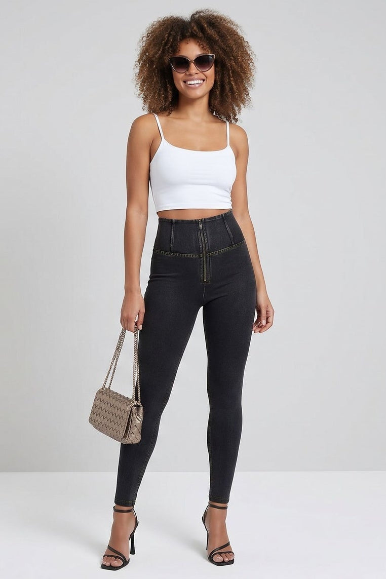 Woman wearing black jeans and a white top, standing against a plain background