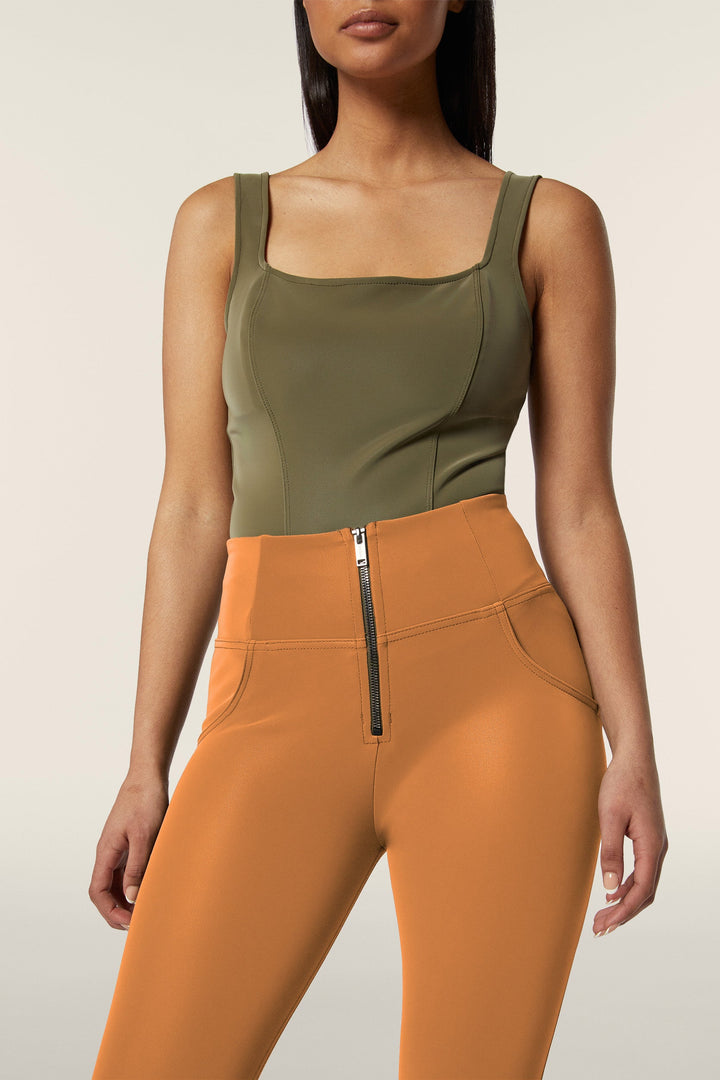 Woman wearing a green tank top and orange high-waisted pants with a zipper.