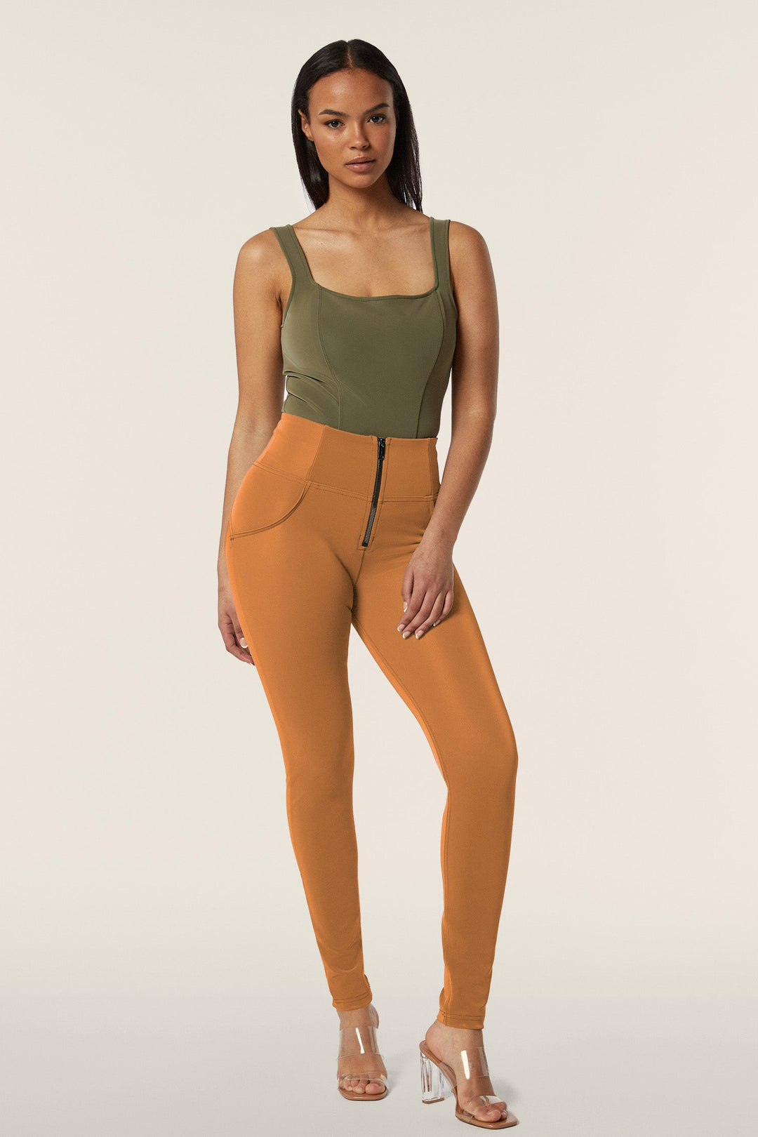 Woman wearing a green tank top and orange leggings on a beige background