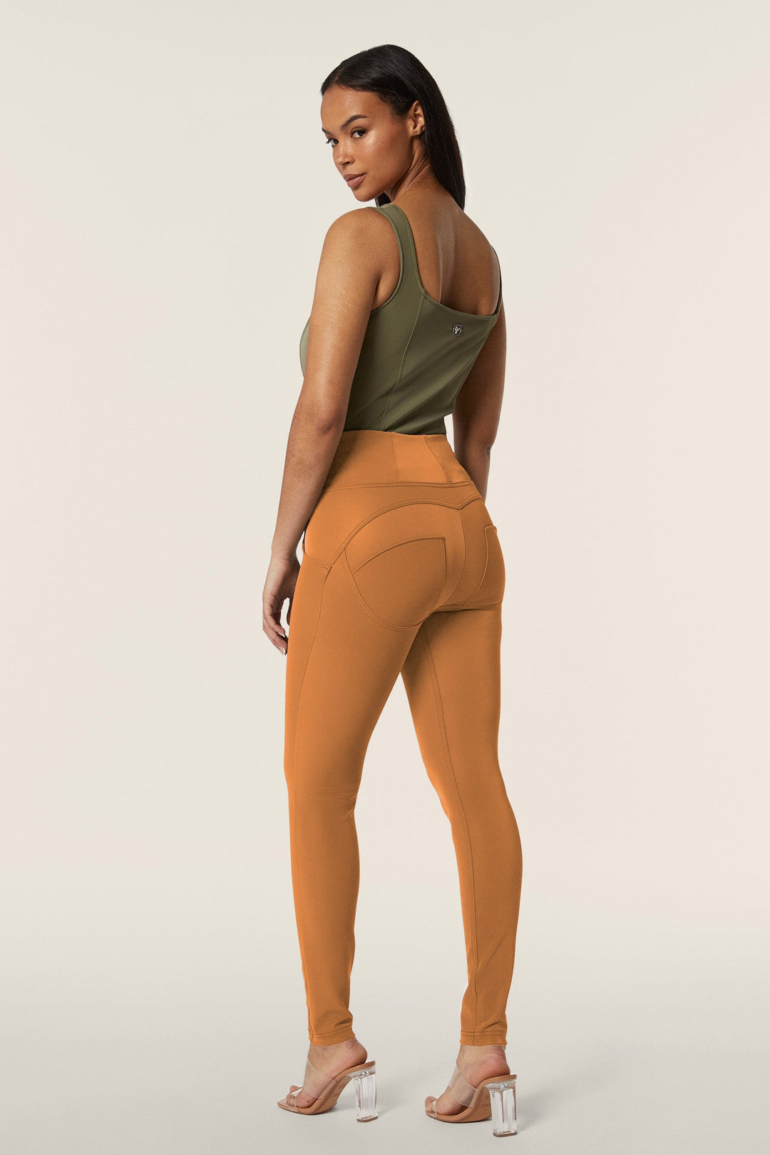 Woman wearing a green tank top and orange leggings on a beige background