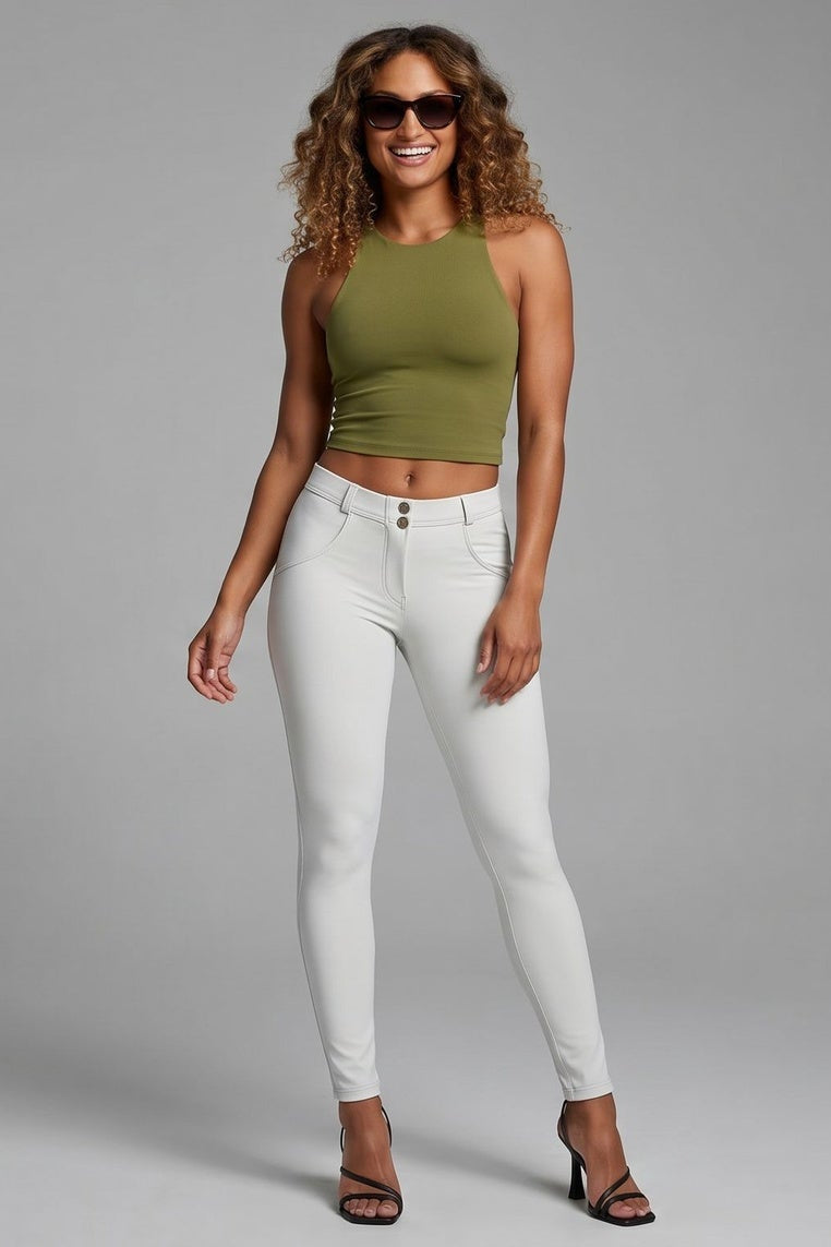Woman wearing a green top and white pants on a gray background