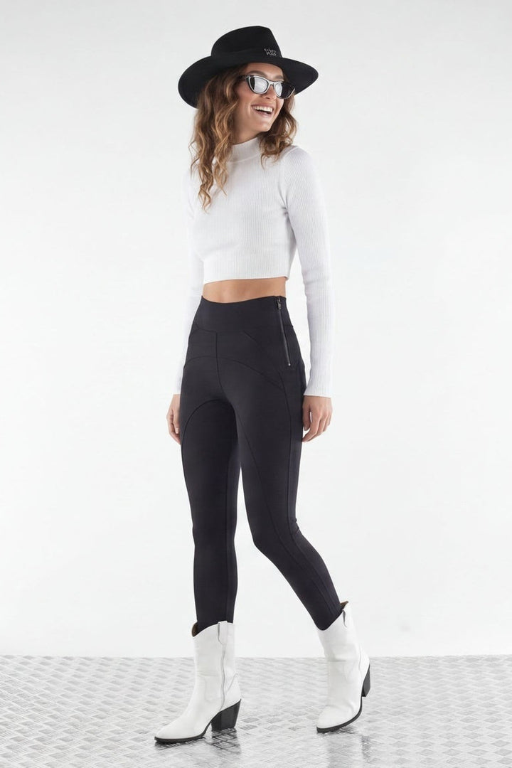 Woman wearing a white top, black leggings, and white boots with a black hat on a white background