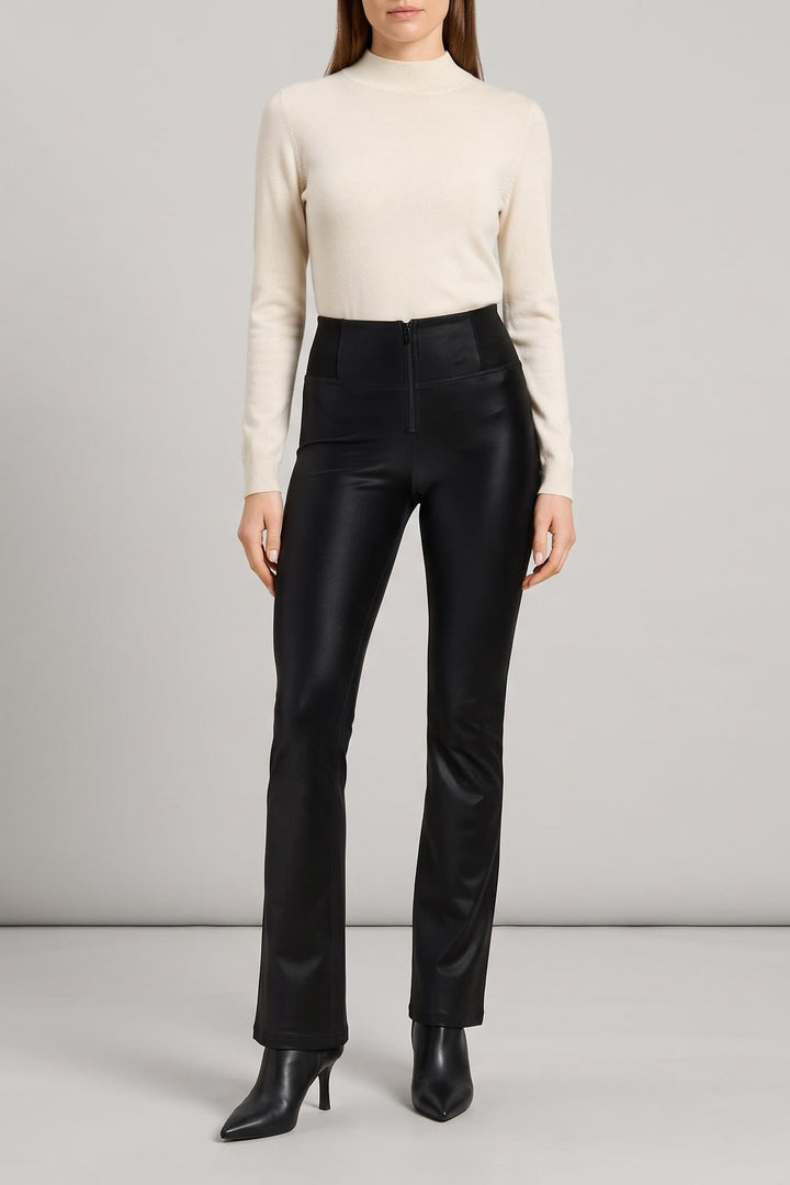 A model wearing a cream mock-neck knit sweater and high-waisted black leather flare pants with black pointed-toe heeled boots, standing against a light gray studio background.
