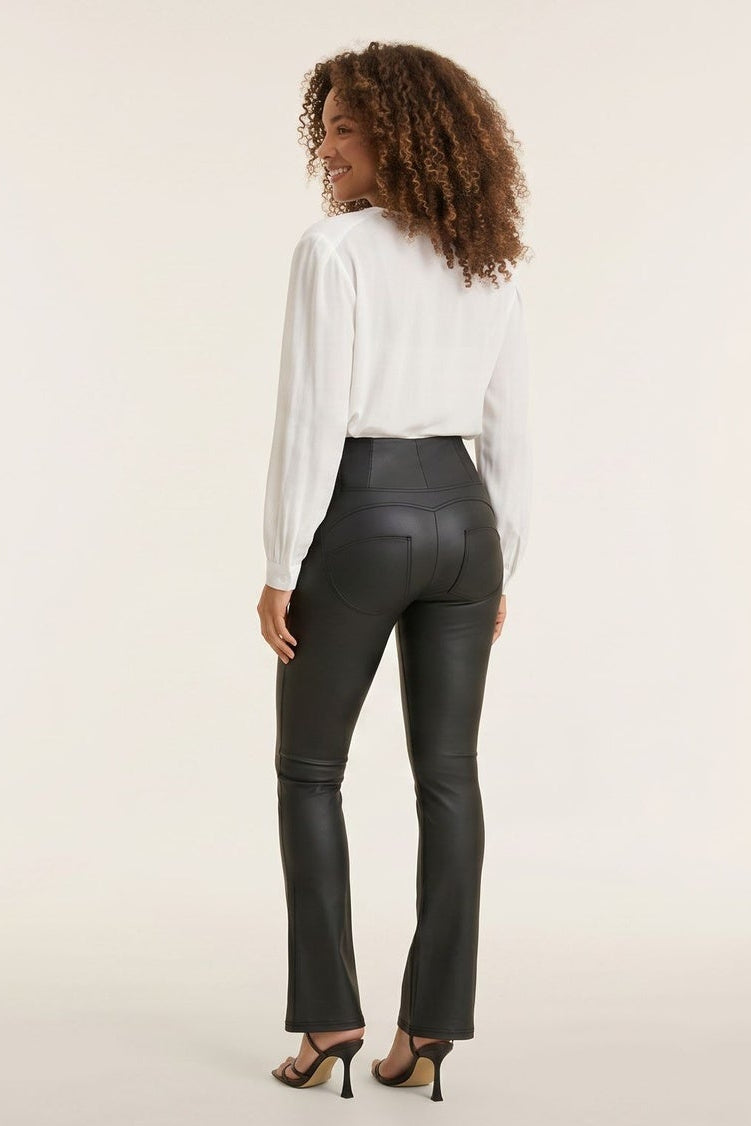 Woman wearing a white blouse and black leather pants, standing against a plain background.