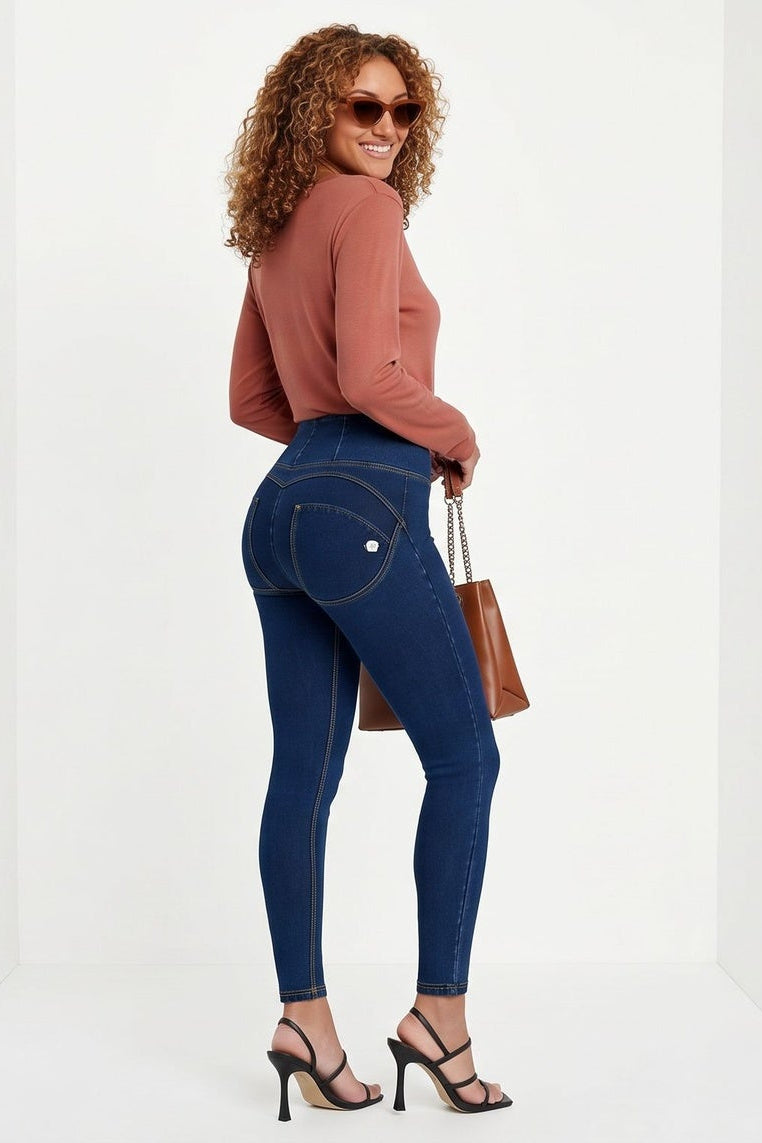 Woman wearing blue jeans and a brown top, holding a brown bag on a white background