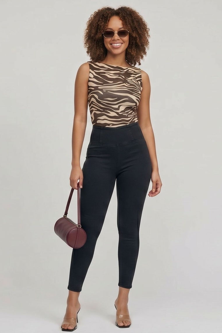 Woman wearing a tiger print top and black pants holding a red handbag on a white background