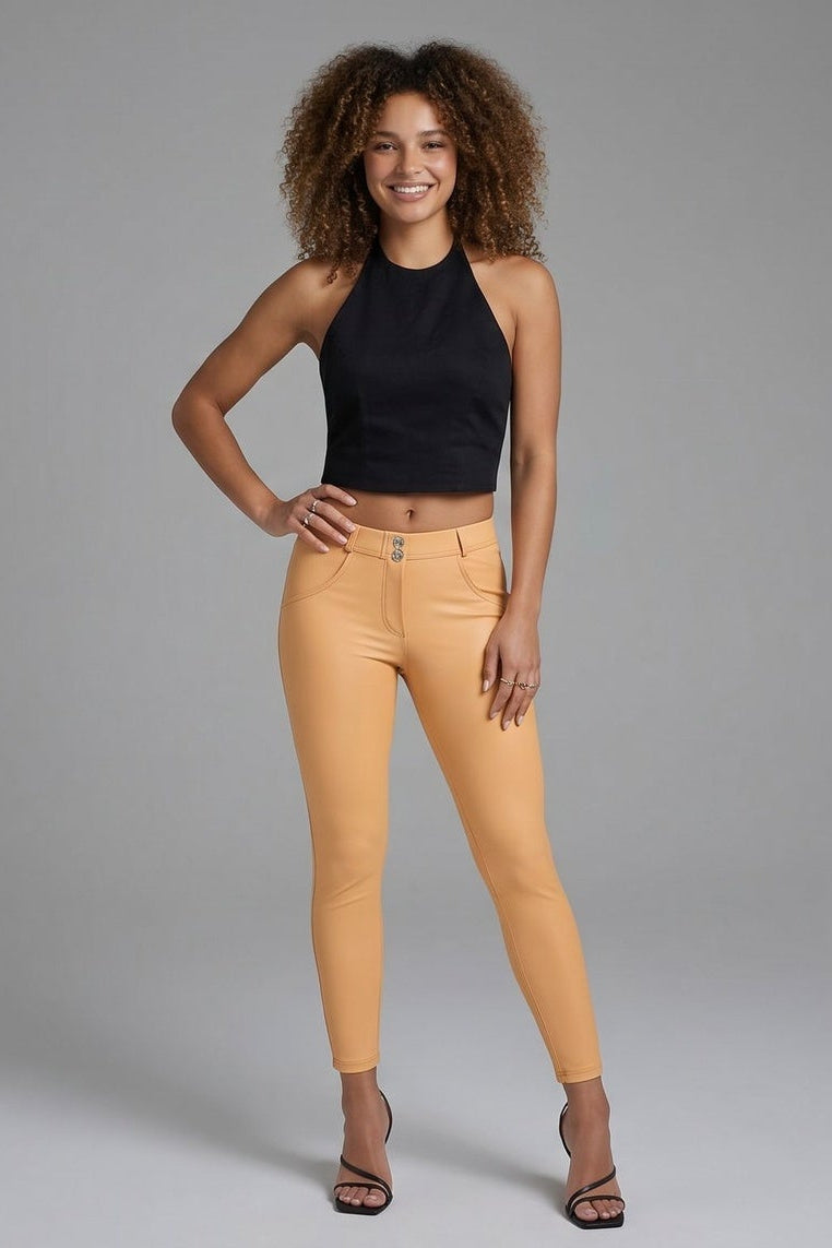 Woman wearing mustard yellow pants and a black top on a gray background