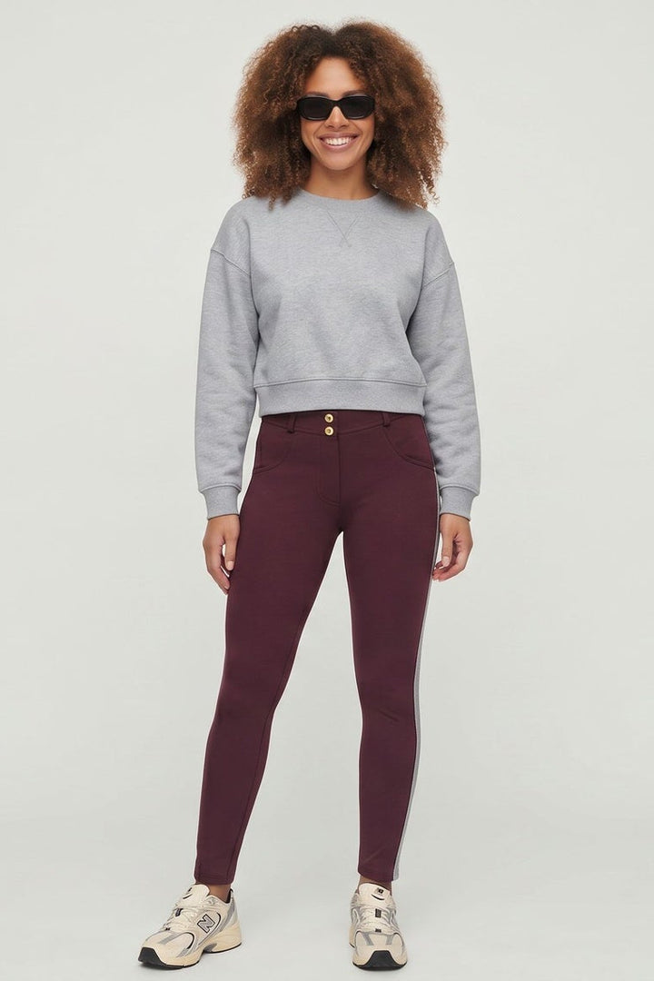 Woman wearing a gray sweatshirt and maroon leggings with white stripes on a white background