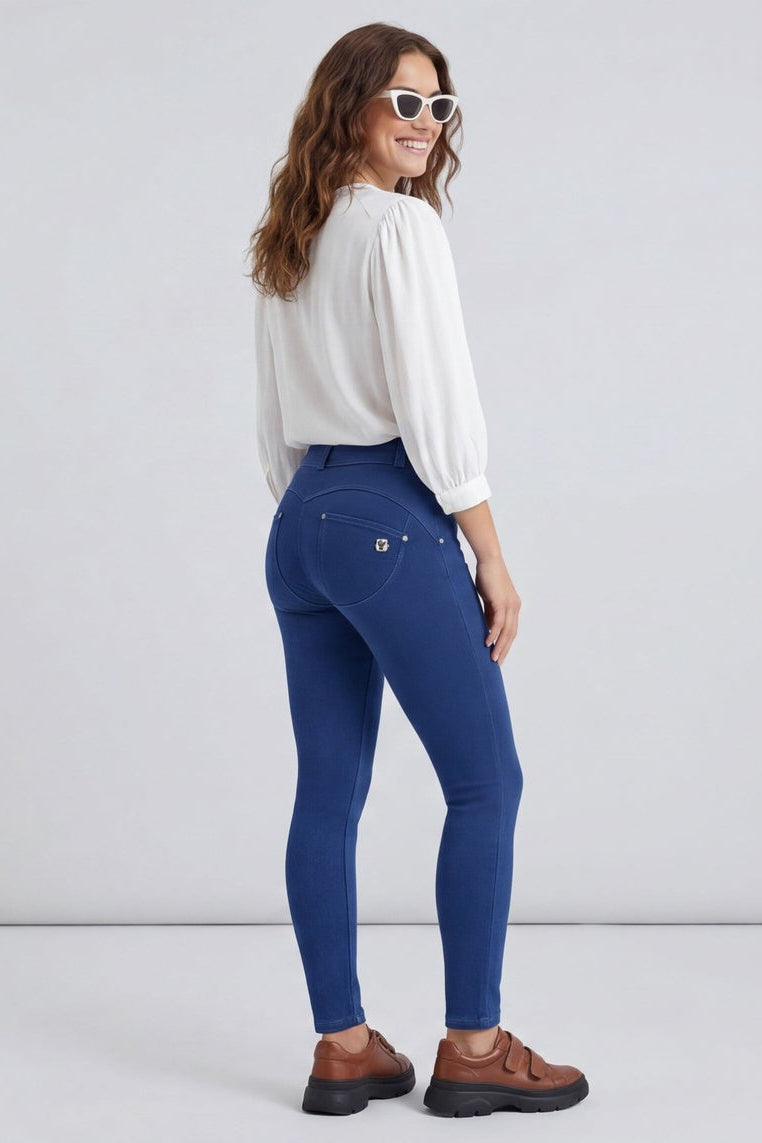 Woman wearing blue jeans and a white shirt, standing against a plain background