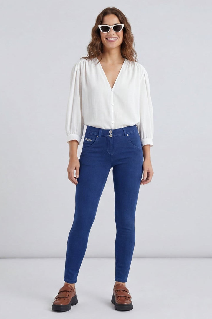 Woman wearing blue jeans and a white shirt, standing against a plain background.