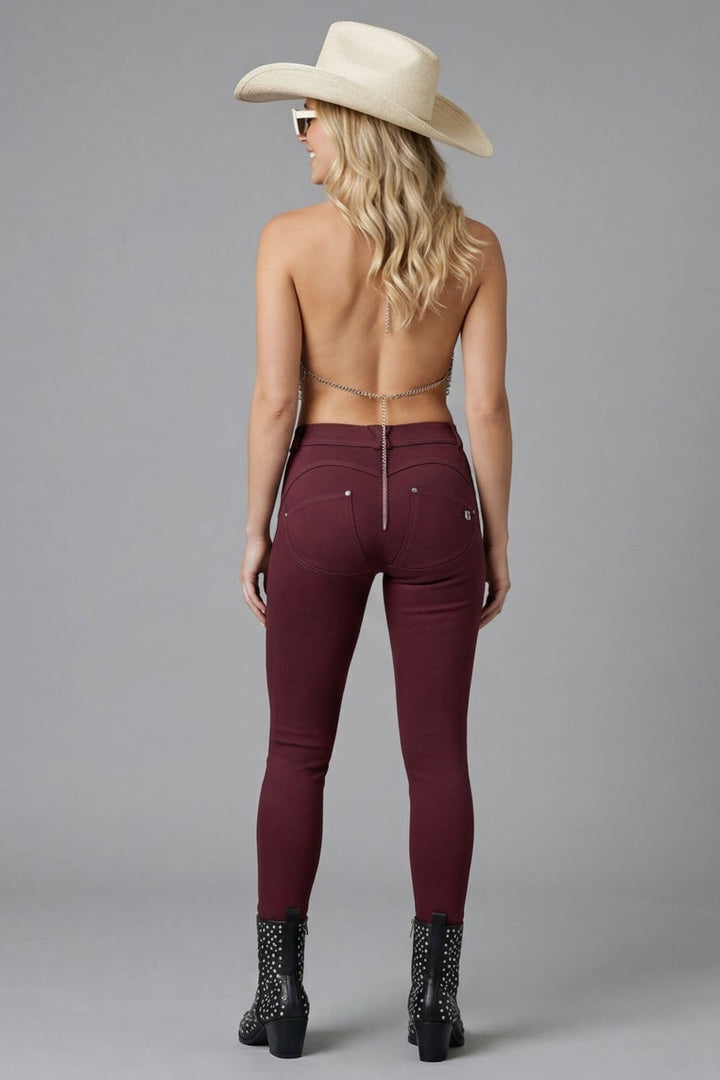 Woman wearing burgundy pants, fishnet top, and cowboy hat on a gray background