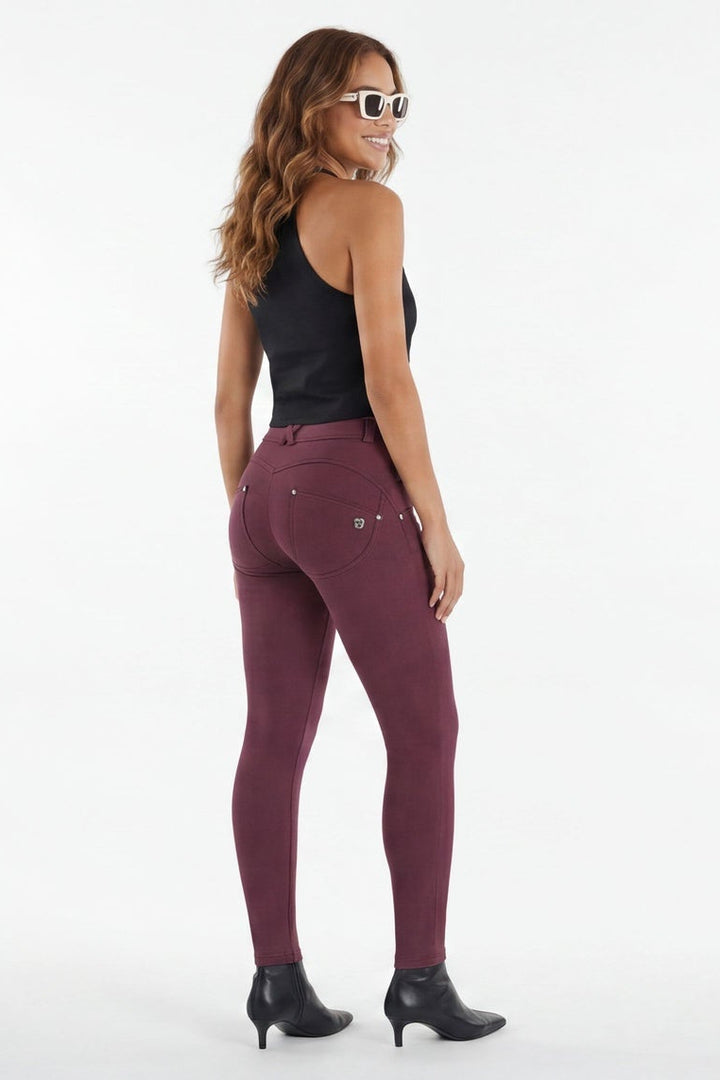 Woman wearing maroon leggings and black top on a white background