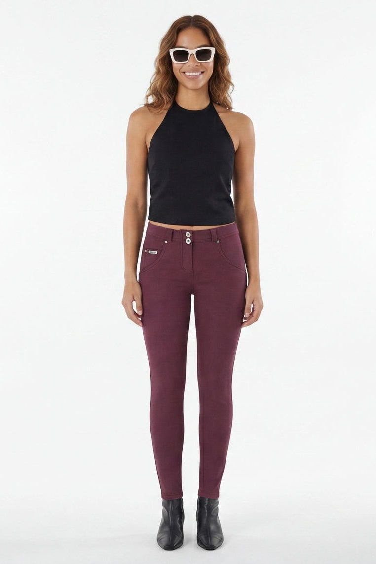 Woman wearing maroon leggings and black top on a white background