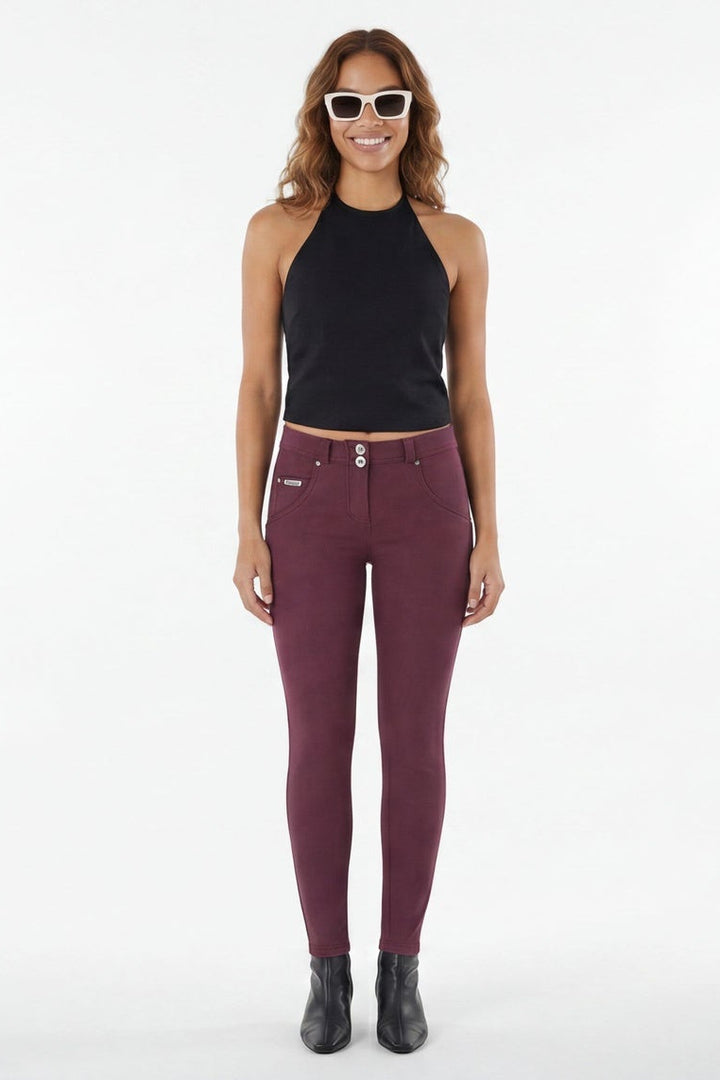 Woman wearing maroon leggings and black top on a white background