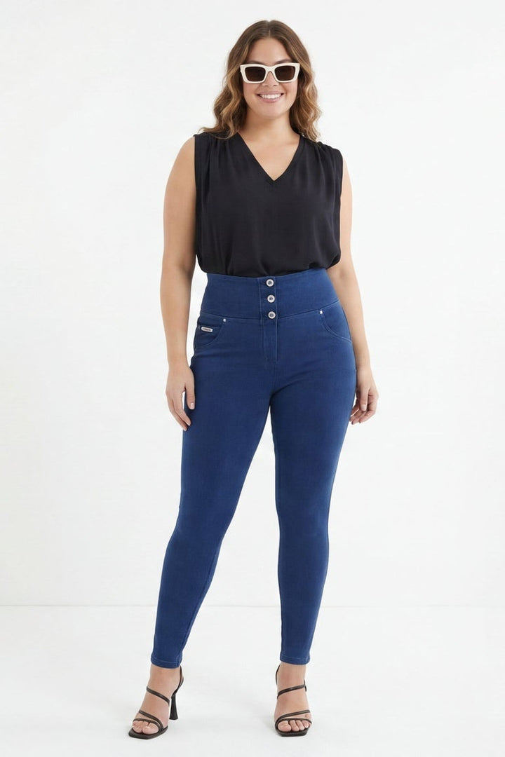 Woman wearing blue jeans and a black top, standing against a white background