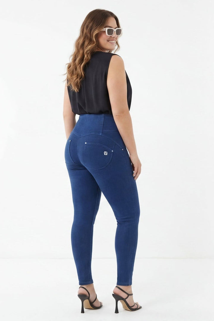 Woman wearing blue jeans and a black top, standing against a white background