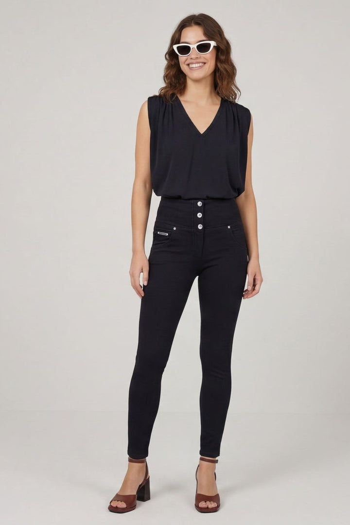 Woman wearing a black sleeveless top and black pants, standing against a plain background.