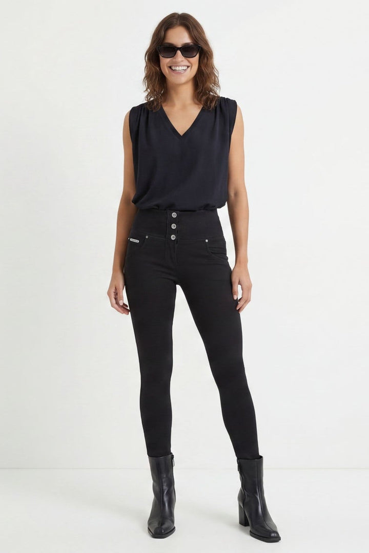 Woman wearing black sleeveless top and pants with buttons on a white background