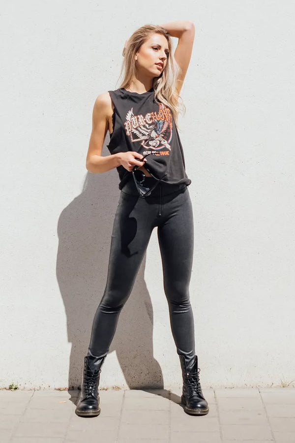 Woman wearing a black sleeveless top and leggings standing against a light gray wall.