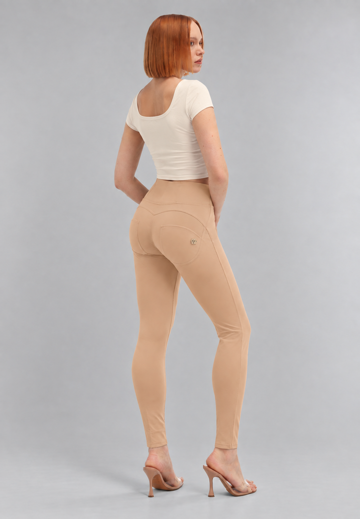 A woman with short red hair is shown from the back wearing beige high-waisted seamless leggings, a white short-sleeve crop top, and nude high-heeled sandals against a light gray studio background.